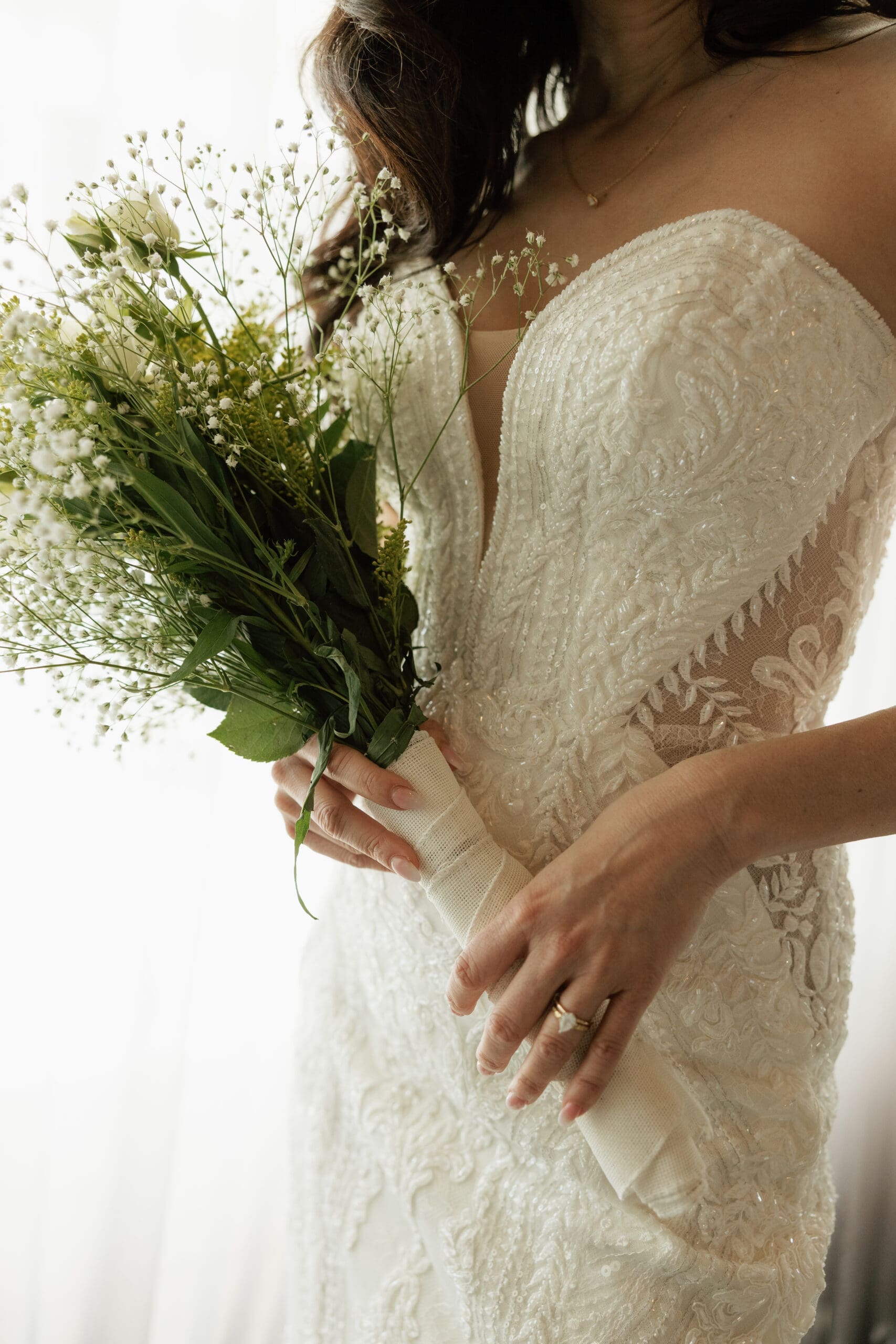 Close-up of bride holding baby's breath bouquet with wedding ring detail in lace gown at Grateful Palate Fort Lauderdale