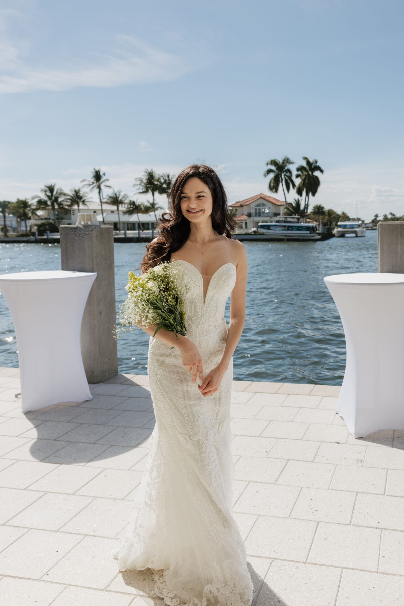 Bride in strapless lace gown smiling with bouquet on waterfront patio at Grateful Palate Fort Lauderdale wedding reception