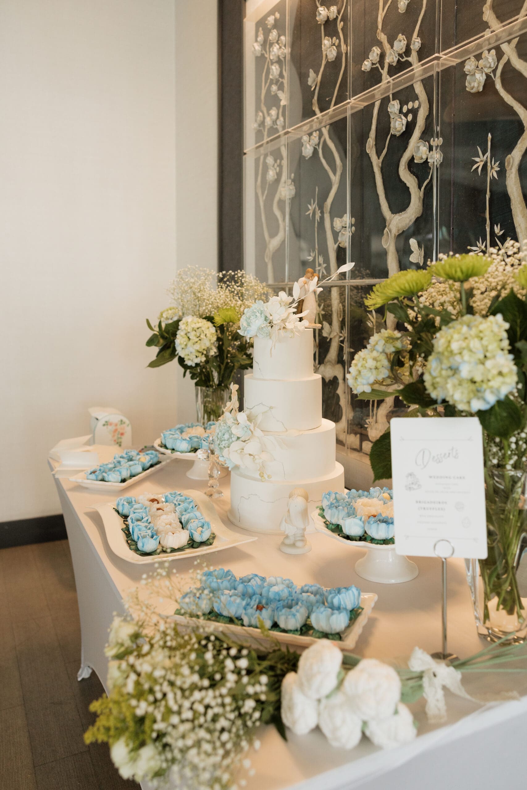 Wedding dessert table with four-tier cake, blue rose sweets, and hydrangea floral arrangements at Grateful Palate Fort Lauderdale